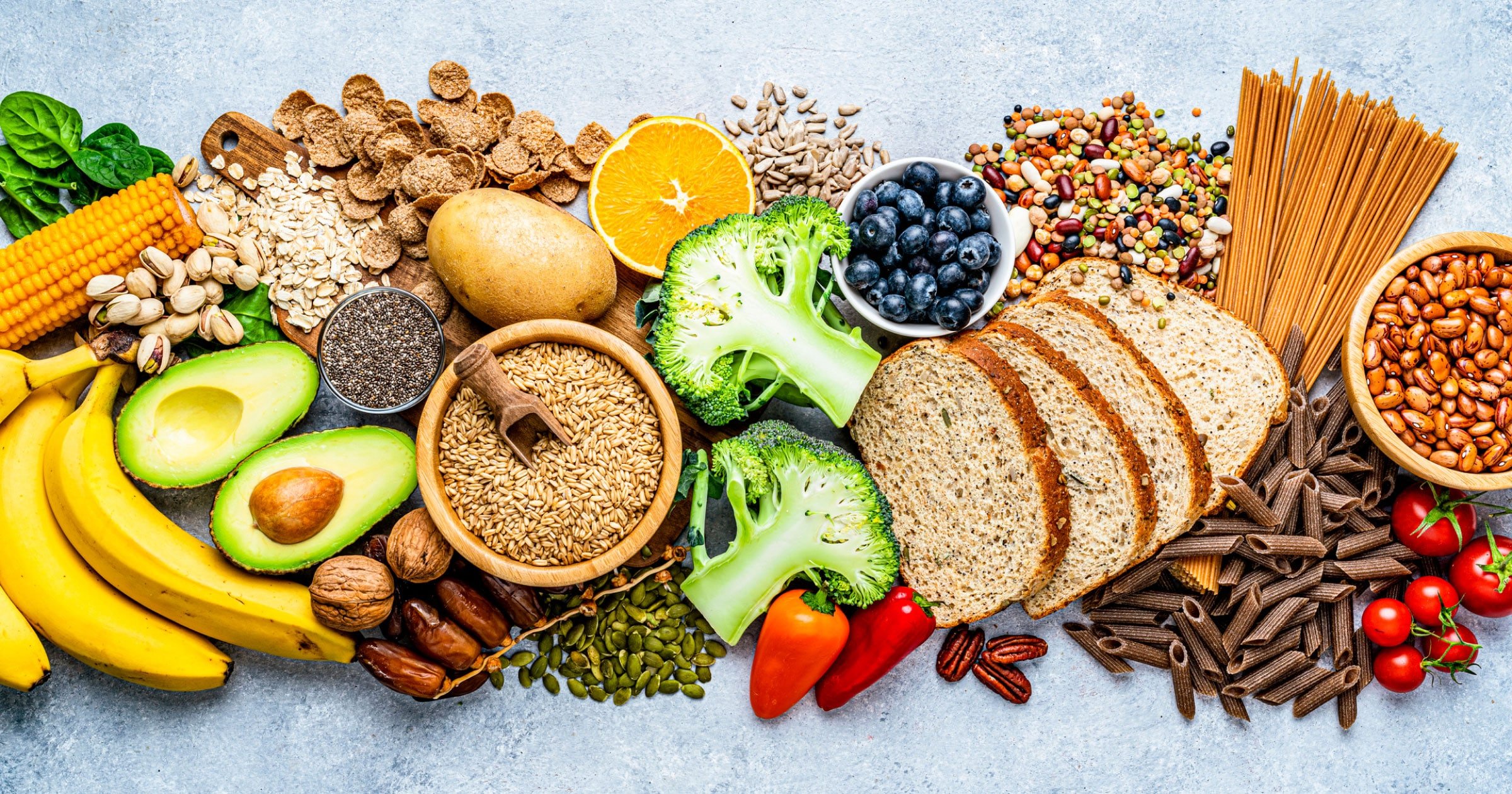 A photo of healthy foods (avocados, whole grains, vegetables, fruit, nuts) gathered together across a clean countertop. 