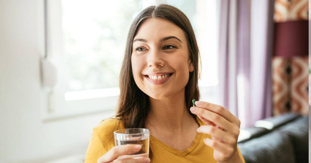 A woman smiling and holding a bottle of prenatal vitamins, highlighting the importance of essential nutrients for fertility and pregnancy health.